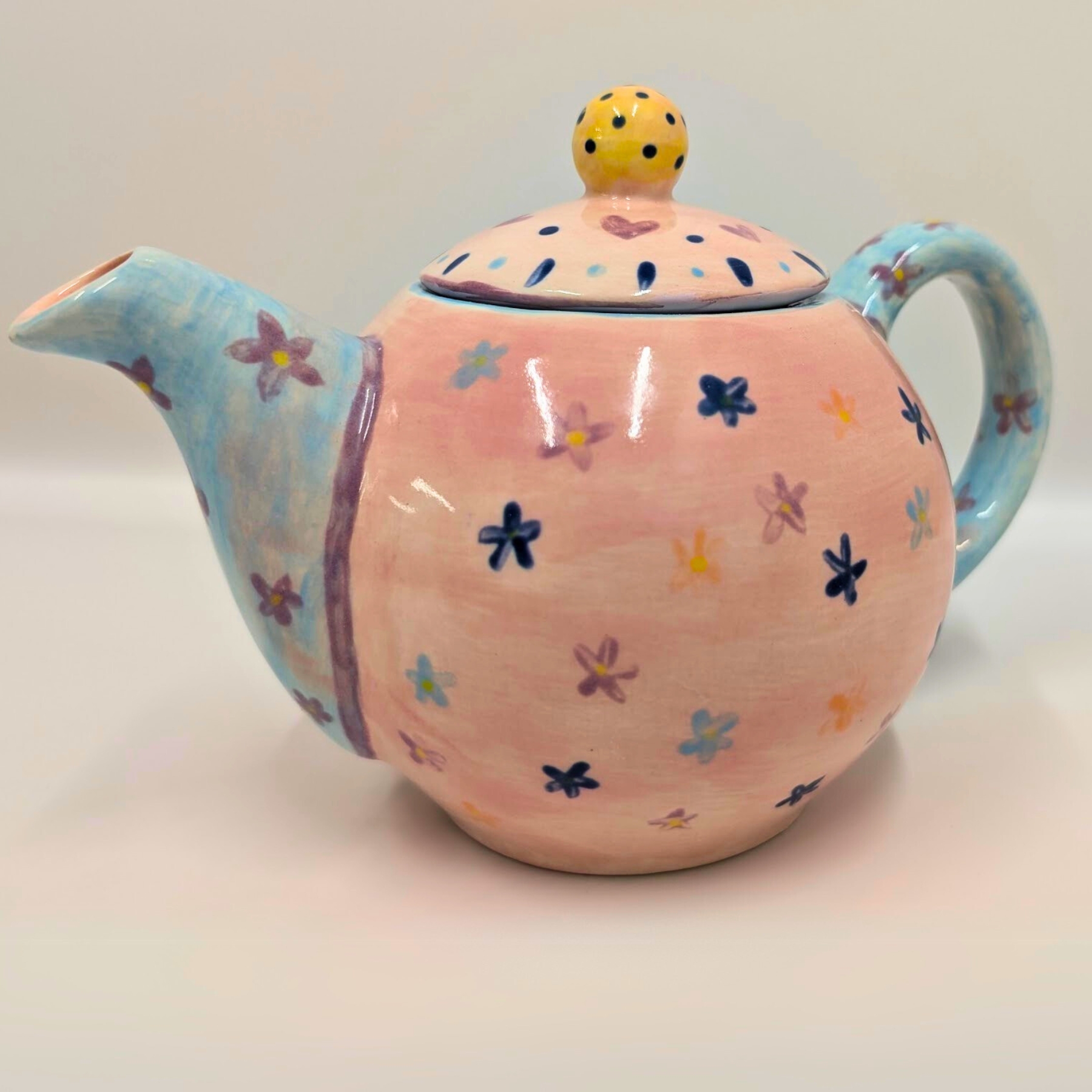 malowanie-ceramiki-gdansk-czajnik09l-kwiaty-rozowo-niebieski Uroczy ceramiczny czajnik o pojemności 0,9l z warsztatów malowania ceramiki w Gdańsku. Różowe naczynie ozdobione kolorowymi kwiatkami w odcieniach niebieskiego, fioletu i żółci, z niebieskim dzióbkiem i uchem oraz żółtą gałką na pokrywce w czarne kropki. Wyjątkowa ręcznie malowana ceramika użytkowa stworzona podczas warsztatów w Gdańsku.