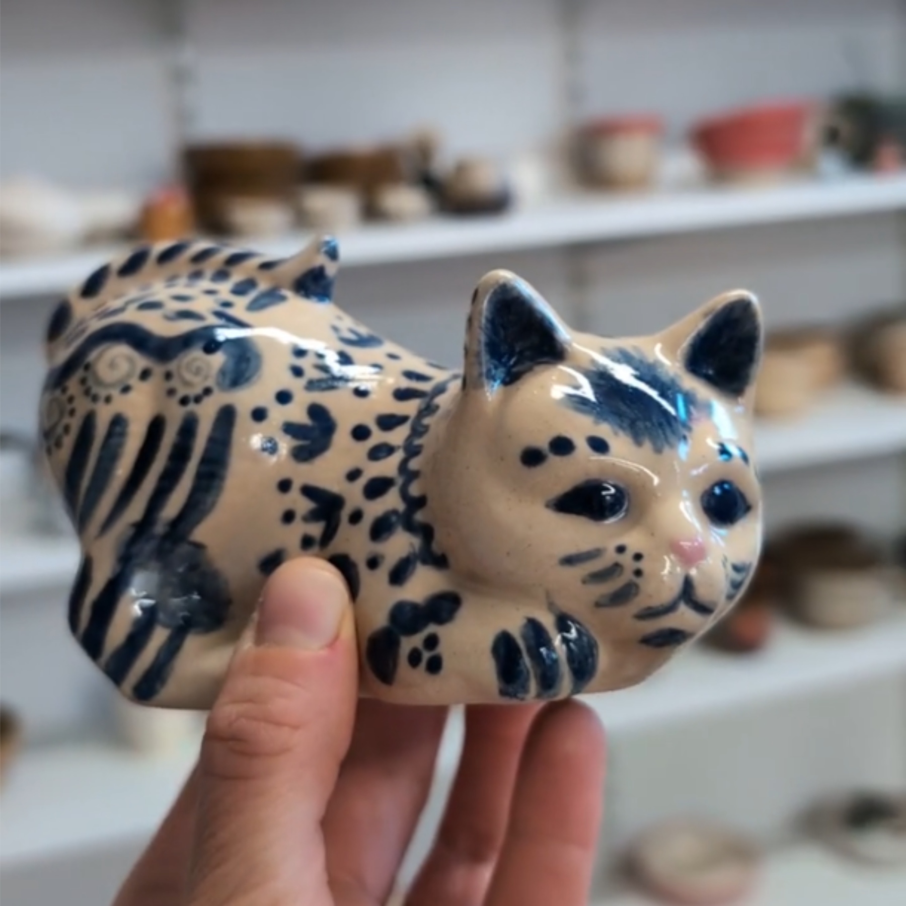 malowanie-ceramiki-gdansk-kot-filemon-kremowy-granatowy Ceramiczna figurka kota o nazwie Filemon z warsztatów malowania ceramiki w Gdańsku. Kremowa figurka z granatowymi wzorami przypominającymi cętki, z różowym noskiem i ekspresyjnymi oczami. Unikatowa ręcznie malowana ceramika wykonana podczas kreatywnych warsztatów w Gdańsku.