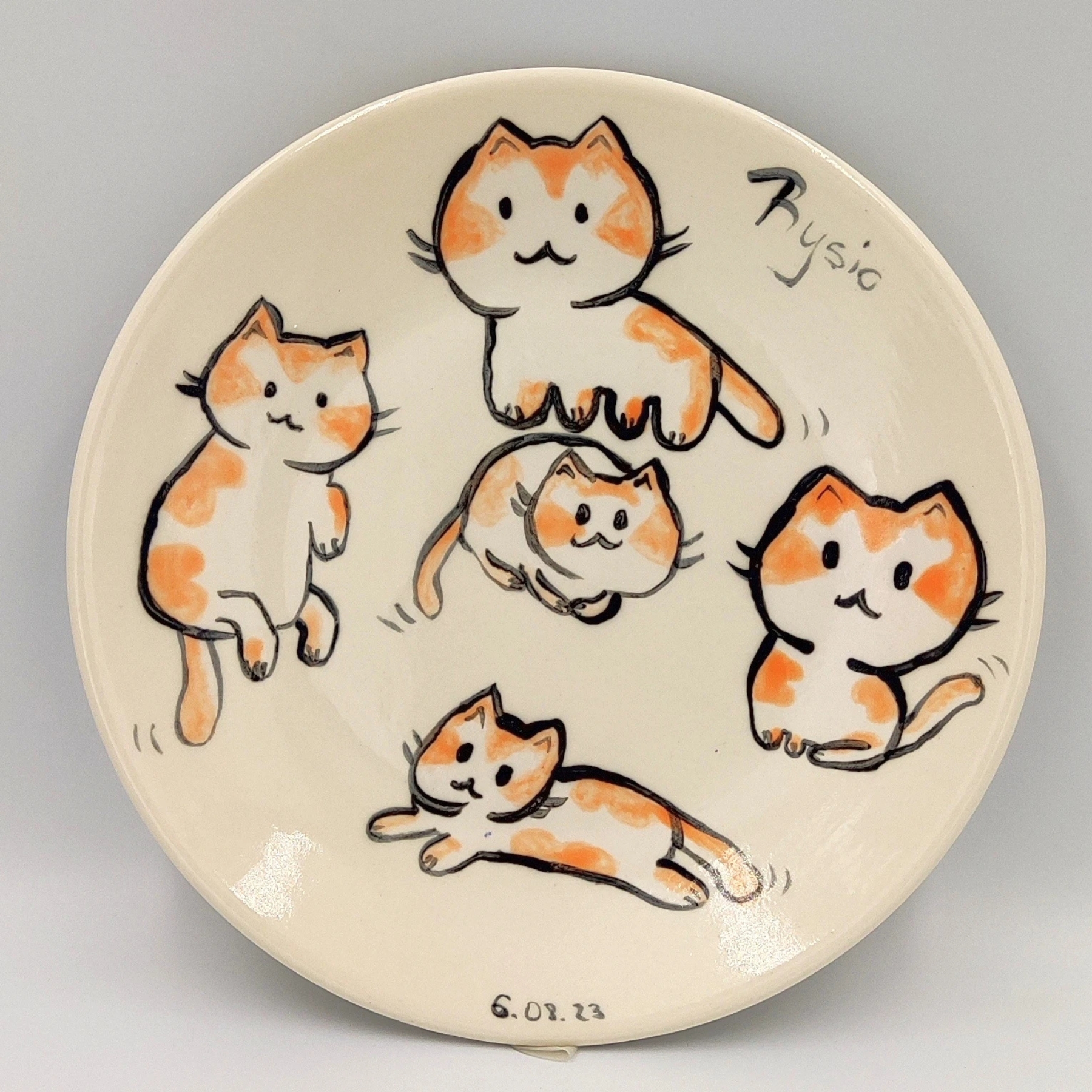 malowanie-ceramiki-gdansk-talerz19cm-koty-rysio-kremowy Ręcznie malowany talerz ceramiczny z warsztatów malowania ceramiki w Gdańsku przedstawiający pięć uroczych pomarańczowych kotów na kremowym tle. Talerz sygnowany imieniem "Rysio" i datą "6.07.23", wykonany podczas kreatywnych warsztatów malowania ceramiki w Gdańsku.