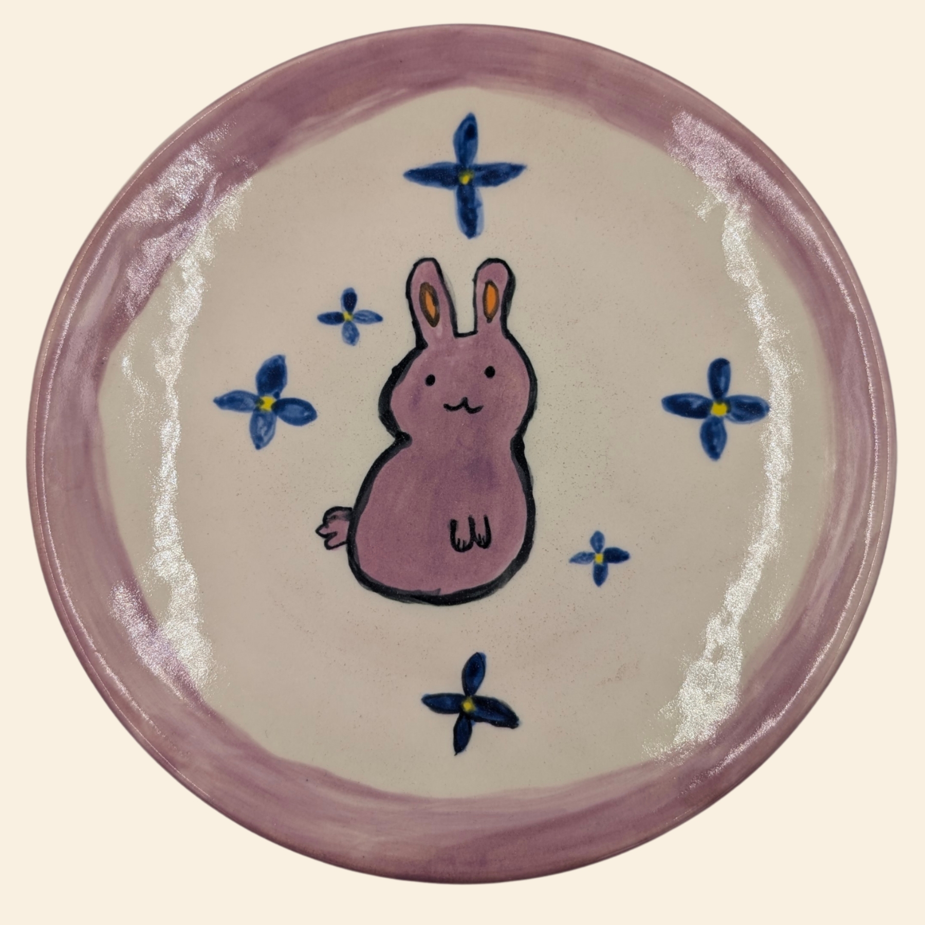 malowanie-ceramiki-gdansk-talerz19cm-krolik-rozowy-kwiaty Ceramiczny talerz z różowym brzegiem z warsztatów malowania ceramiki w Gdańsku, przedstawiający uroczego różowego królika otoczonego niebieskimi kwiatkami z żółtymi środkami. Unikatowy projekt stworzony podczas warsztatów malowania ceramiki w Gdańsku.