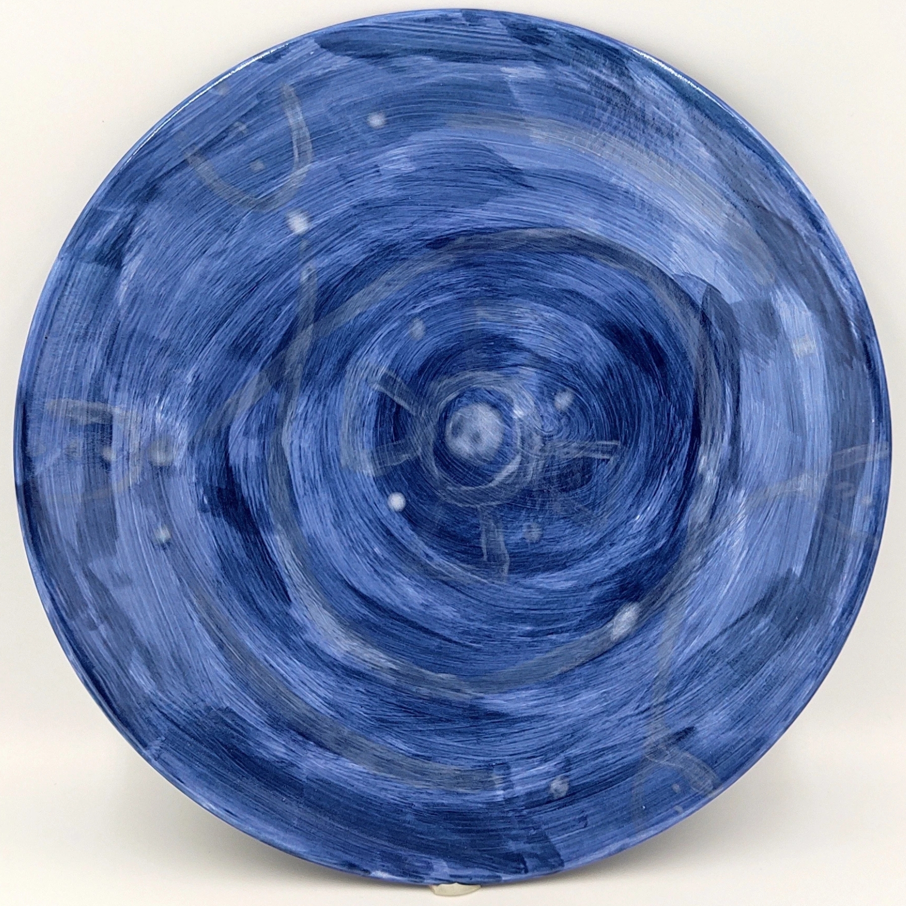 malowanie-ceramiki-gdansk-talerz25cm-niebieski-spiral Talerz ceramiczny pomalowany w różnych odcieniach niebieskiego z wzorem spiralnym promieniującym od środka. Szkliwiona powierzchnia tworzy dynamiczny, hipnotyczny efekt z jaśniejszymi niebieskimi akcentami na ciemnoniebieskim tle